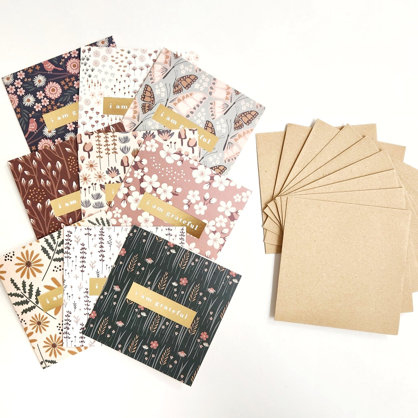 The Florals Gratitude Mini Note Card Set by Maylay Co. showcases a range of premium quality greeting cards adorned with diverse floral designs and the phrase "I am grateful" elegantly stamped in gold foil. The set includes a stack of plain brown envelopes, all presented on a simple white background.