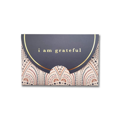 Introducing the So Delicate 6 Pk Gift Card Envelopes by Maylay Co., featuring an elegant scalloped flap and a sophisticated premium matte finish. The black upper section is adorned with a striking gold foil design that reads "I am grateful," while the lower section showcases a decorative pattern in pink, gold, and black. Ideal for use as gift card holders.