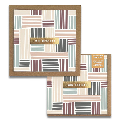 The Basketweave Gratitude Greeting Card from Maylay Co. showcases a square design with a geometric pattern of stripes in subtle shades of pink, green, brown, and beige. The front displays the message "i am grateful" on a gold background. An additional small card attached suggests giving it as an expression of thanks.