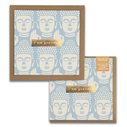 The "Be Still Gratitude Greeting Card" by Maylay Co. features a high-quality design with a repeating pattern of Buddha faces in beige on a light blue background. Centered on the card is a gold-foiled message that reads, "I am grateful." Ideal for collectors of gratitude cards, it includes a matching brown envelope.