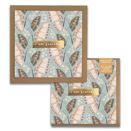 A square greeting card from the Butterfly Gratitude Greeting Cards by Maylay Co. displays a floral and butterfly design in pastel hues. It includes the text "I am grateful" in gold lettering on a brown background, artistically packaged for presentation.