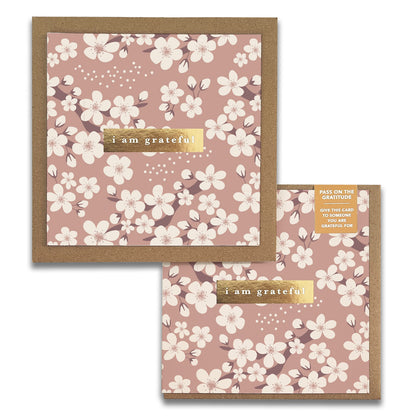 The Cherry Blossoms Gratitude Greeting Cards by Maylay Co. are square and showcase white flowers against a pink background, making them ideal for expressing genuine appreciation. The front features the phrase "I am grateful" in elegant gold lettering. As part of our Gratitude Cards collection, it is packaged to inspire you to share it as a considerate gesture.