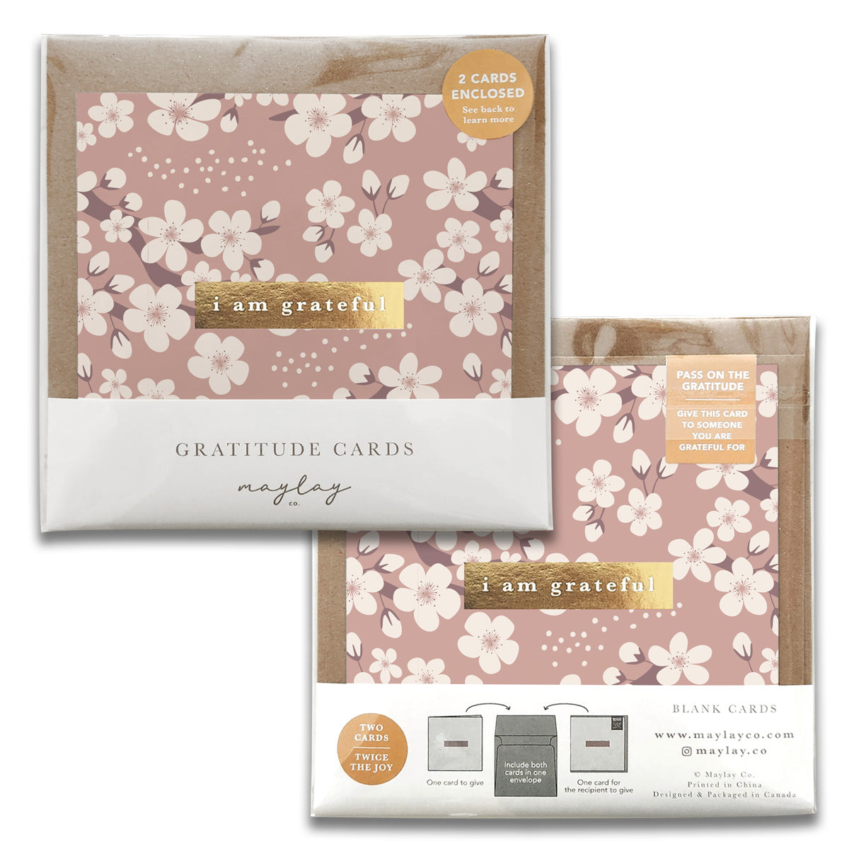 A pair of Cherry Blossoms Gratitude Greeting Cards from Maylay Co., embellished with a floral pattern set against a pink backdrop and showcasing the phrase "I am grateful." The packaging includes two greeting cards along with information about the brand, Maylay Co., and an uplifting message encouraging the sharing of gratitude.