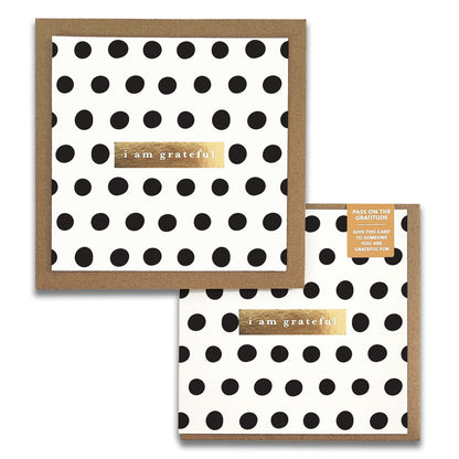 The Dots Monochrome Gratitude Greeting Card from Maylay Co. features a white design with black polka dots and is enhanced by a gold rectangular sticker that reads "I am grateful." This card, perfect for expressing heartfelt thanks, comes with a matching brown envelope.