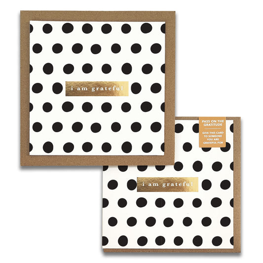 The Dots Monochrome Gratitude Greeting Card from Maylay Co. features a white design with black polka dots and is enhanced by a gold rectangular sticker that reads "I am grateful." This card, perfect for expressing heartfelt thanks, comes with a matching brown envelope.