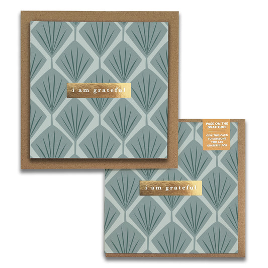 The Fans Floral Gratitude Greeting Card by Maylay Co. showcases a square design featuring a geometric leaf pattern in muted teal tones, crafted from premium materials. It includes a gold embossed label reading "I am grateful" at the center. A smaller version in the corner bears the tag "Pass on the Gratitude," making it ideal for expressing gratitude-inspired sentiments.