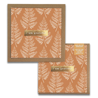 The two Fern Gratitude Greeting Cards by Maylay Co. feature brown designs with white fern patterns and a gold foil label reading "I am grateful." One card is angled in the background, while the other is displayed straight on in the foreground, with a corner of its envelope visible.