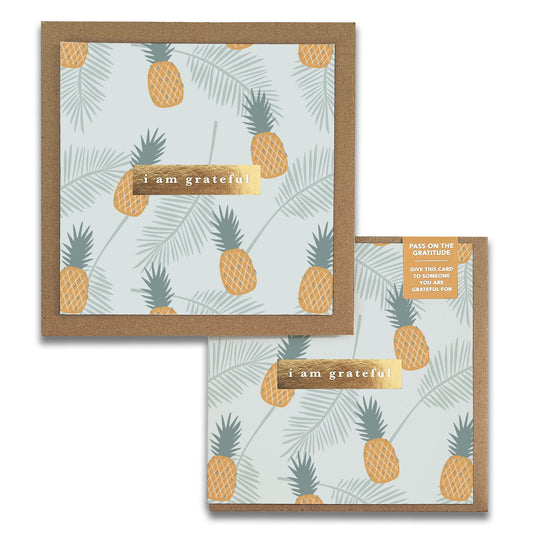 The charming Golden Gratitude Greeting Cards by Maylay Co. showcase a design of pineapples and palm leaves on a light background, with the phrase "I am grateful" prominently displayed. An additional card slightly overlaps the main one, adding an elegant touch to this ideal Thank You note collection.