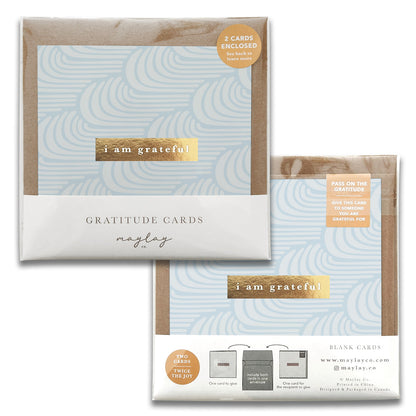 The image shows two packages of light blue High Tides Gratitude Greeting Cards, decorated with swirling designs. Inside each package are two greeting cards, each with a gold sticker that says "I am grateful." The gratitude-inspired collection is branded as Maylay Co., which is prominently displayed on the packaging.