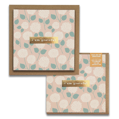 The Hydrangeas Floral Gratitude Greeting Cards by Maylay Co. feature a beautiful floral pattern with white flowers and green leaves on a beige background, elegantly highlighted with "Thank You" in a gold box. A smaller Gratitude Card complements the set, reflecting the same design and providing instructions for sharing your gratitude.