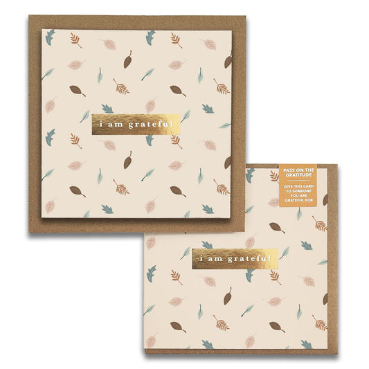 Two aesthetically pleasing greeting cards from Maylay Co., known as Leaves Gratitude Greeting Cards, showcase a beige background adorned with scattered leaf patterns in muted colors. These gratitude cards feature a label with gold borders that reads "I am grateful," accompanied by a tag encouraging you to pass the thank you card to someone who deserves your appreciation.