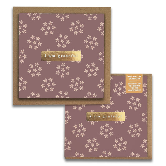 The Posy Floral Gratitude Greeting Cards by Maylay Co. include two cards adorned with a floral pattern on a brown background. Each card features the phrase "I am grateful" highlighted on a gold strip. An accompanying tag encourages, "PASS ON THE GRATITUDE, GIVE THIS CARD TO SOMEONE YOU ARE GRATEFUL FOR." These are perfect for expressing thanks as greeting cards.