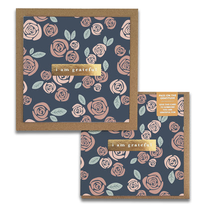 Roses Gratitude Greeting Cards by Maylay Co. feature a floral pattern of pink roses and green leaves set against a dark blue background. The center of the card includes a label that reads "I am grateful." When opened, the card reveals a matching design inside, making it ideal for expressing heartfelt appreciation.