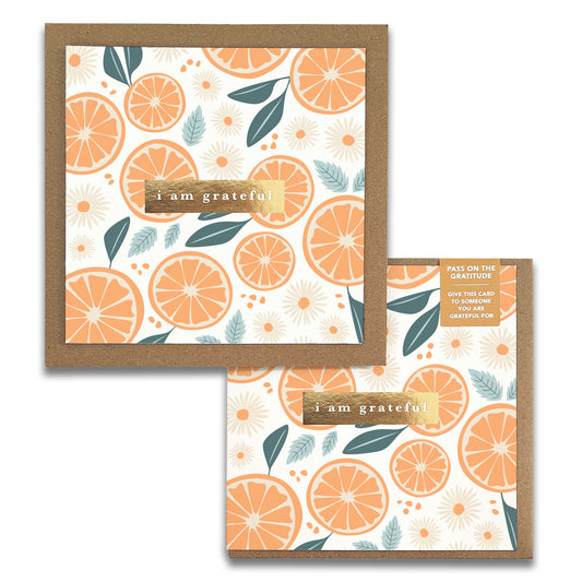 Introducing the Tang Gratitude Greeting Cards by Maylay Co., featuring a square design embellished with vivid orange slices, leaves, and daisies on a pure white background. At the center, the message "I am grateful" beautifully conveys sincere appreciation. This sophisticated greeting card comes complete with an accompanying envelope.