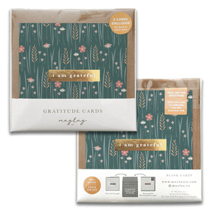 Introducing the Wildflowers Gratitude Greeting Cards by Maylay Co. These elegant cards feature a floral design with the phrase "I am grateful." Available in a package of two, they showcase a lush green background adorned with pink and white flowers accompanied by grass patterns, making them perfect for any heartfelt thank you.