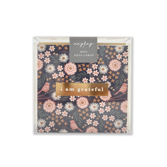 A set of Florals Gratitude Mini Note Cards features a premium quality floral design with pink and white flowers against a dark background. The phrase "i am grateful" is elegantly printed in the center using a gold foil stamp design, while the brand name Maylay Co. is displayed at the top.